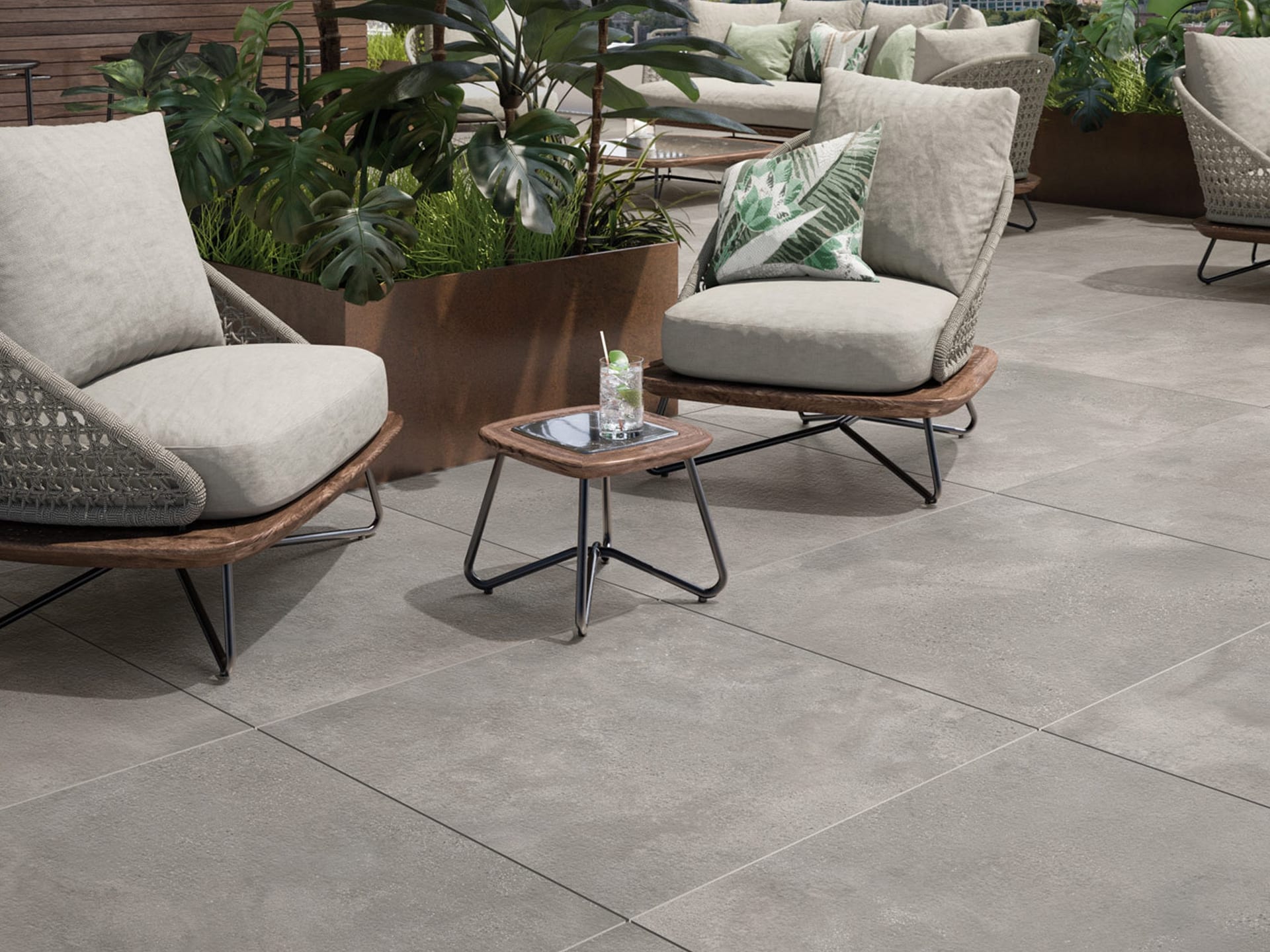 Terrasse mit gepolsterten Stühlen, Fliesenboden, kleinem Tisch und großen Topfpflanzen im Hintergrund